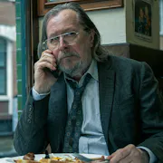 A bedraggled middle aged white man in a tired suit eating a fry up at a greasy spoon café while on the phone