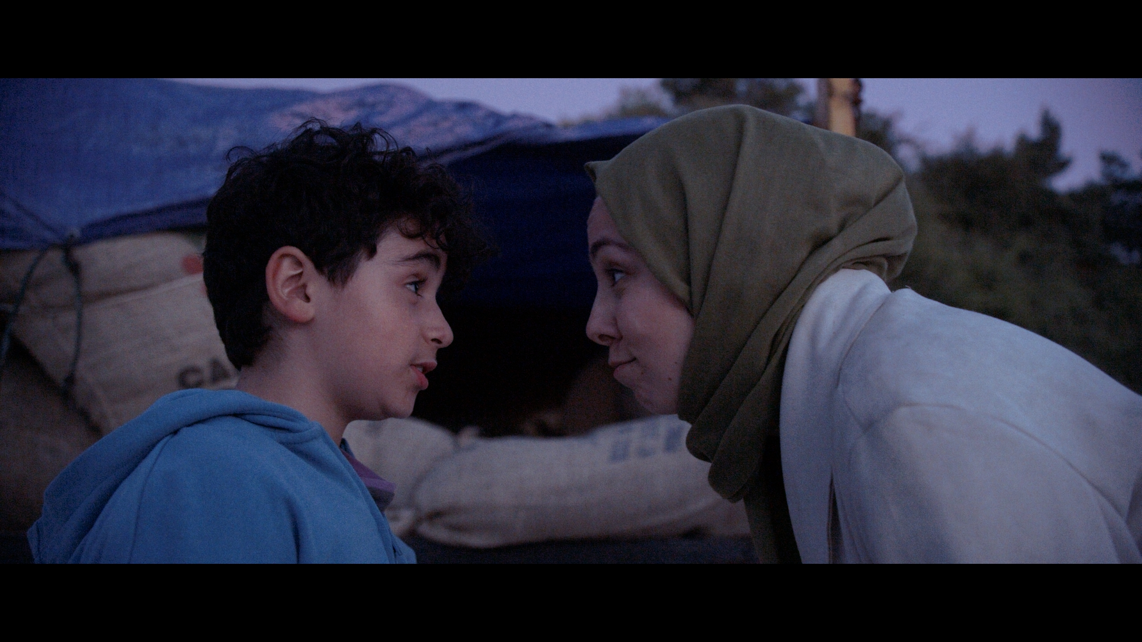 A woman with a headscarf is talking closely to a little boy in a blue jumper
