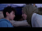 A woman with a headscarf is talking closely to a little boy in a blue jumper