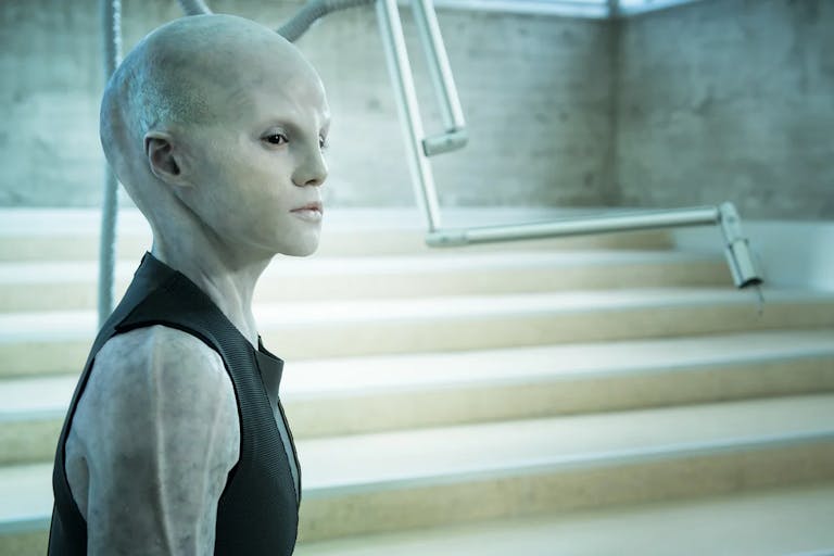 A fish-like personis standing and looking way from the camera