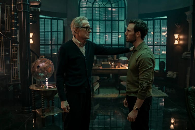 A middle aged white man wearing glasses and a cardigan stands with his hand on the should of a young white man