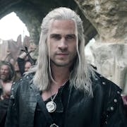 A white man with long white hair and hazel eyes, wearing black leather and a sword strapped to his back