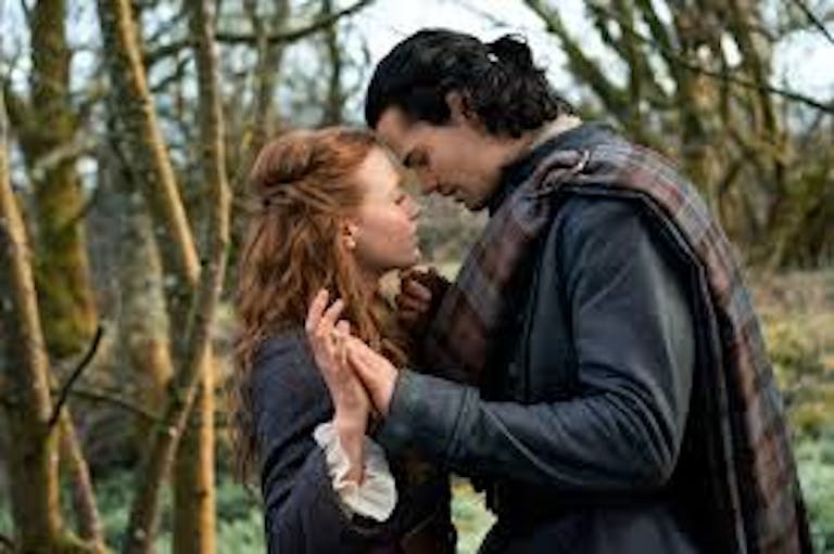 A man and a woman embracing in the woods. The man is wearing dark tartan