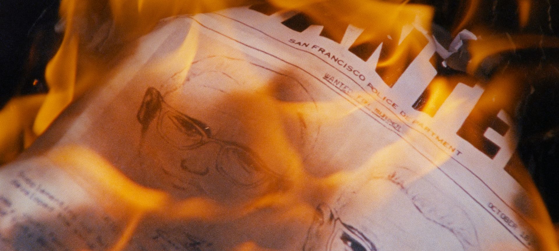 Newspaper article with a sketch of a man's face on it set alight with orange flames