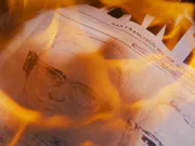 Newspaper article with a sketch of a man's face on it set alight with orange flames