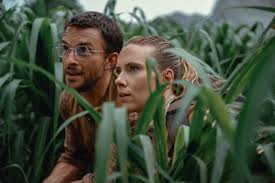 A blonde woman and a man with glass are crouching in some tall vegetation.
