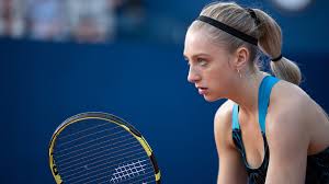 A blonde woman is holding a racket in a position ready to receive a ball