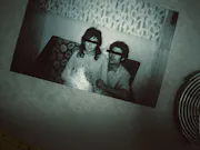 A black and white photo of two people with their eyes crossed out as if redacted sits on a table with