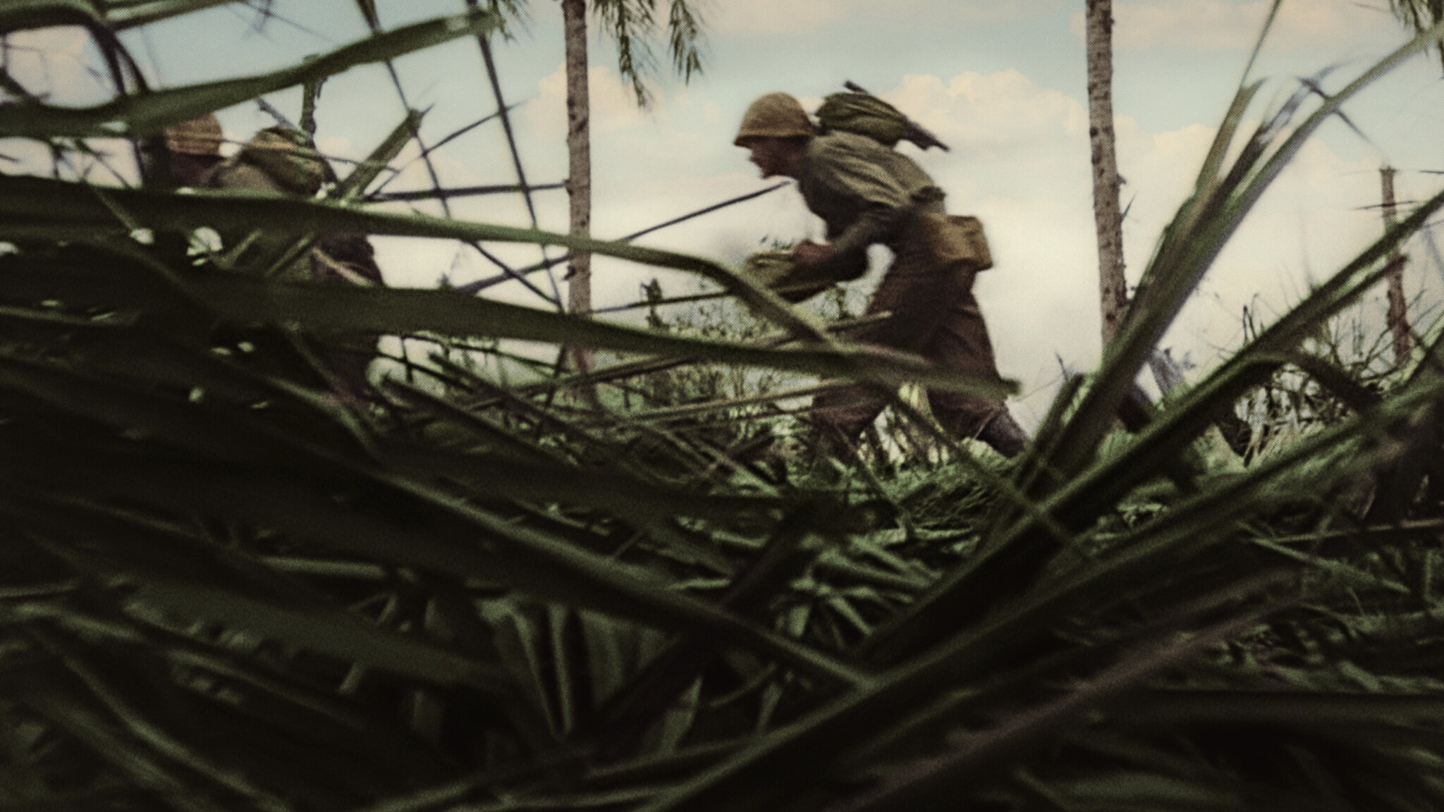 A soldier can be seen running in full gear at a distance. The shot is from ground level behind with grass seen on the foreground