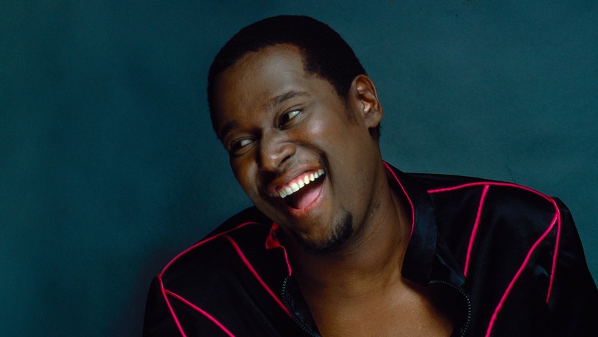 A Black Man in a black jacket with bright red lines is laughing and leaning to his right