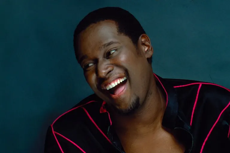 A Black Man in a black jacket with bright red lines is laughing and leaning to his right