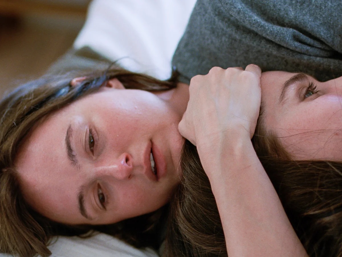 A close up of a woman, lying down, holding another woman’s head to her chest.