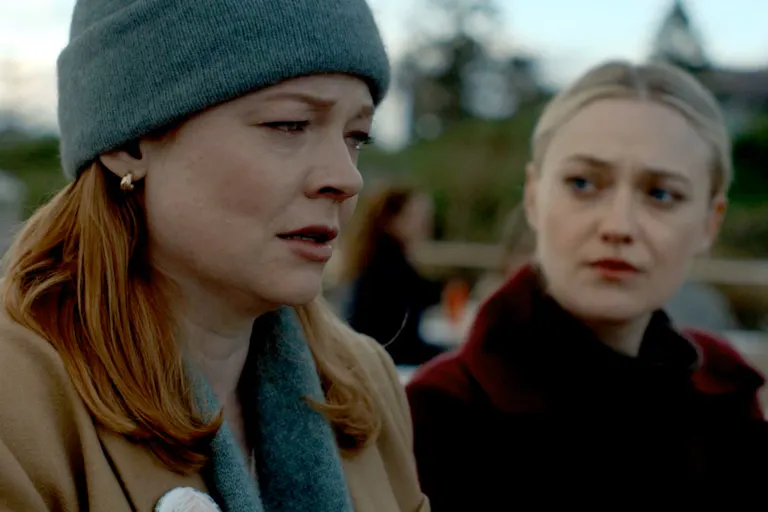 A close-up of Marissa Irvine, played by Sarah Snook, and Jenny Kaminski, played by Dakota Fanning. They are outside. Marissa is wearing a grey hat, scarf and a camel coat. She looks upset. Jenny, wearing a claret coloured coat looks sympathetically at Marissa.