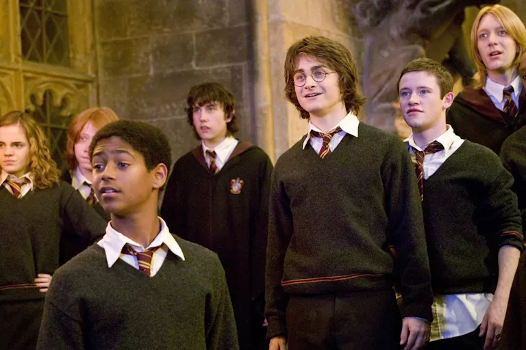A young group of students in jumpers, ties and robes standing inside a grand castle