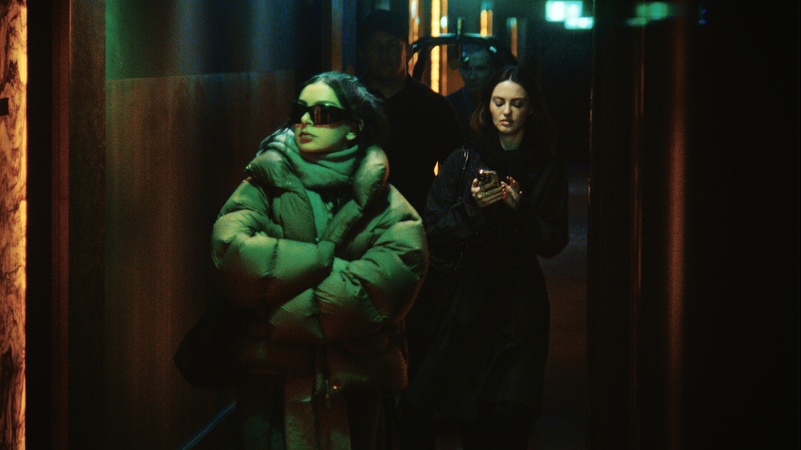 A young woman in oversized glasses and puffer coat walk with an entourage behind her