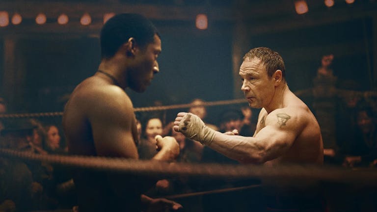 A young Black man and an older white man circle each other in a boxing ring