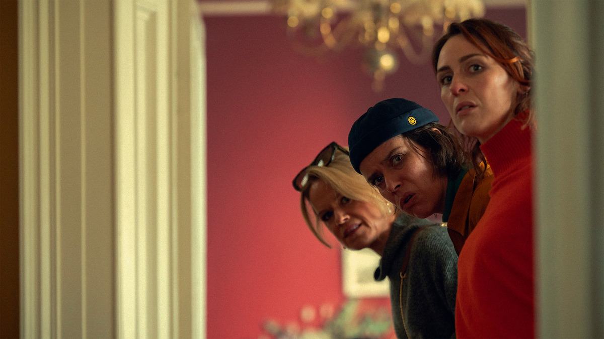 Three white women peeking round a door with a suspicious look on their faces