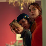Three white women peeking round a door with a suspicious look on their faces