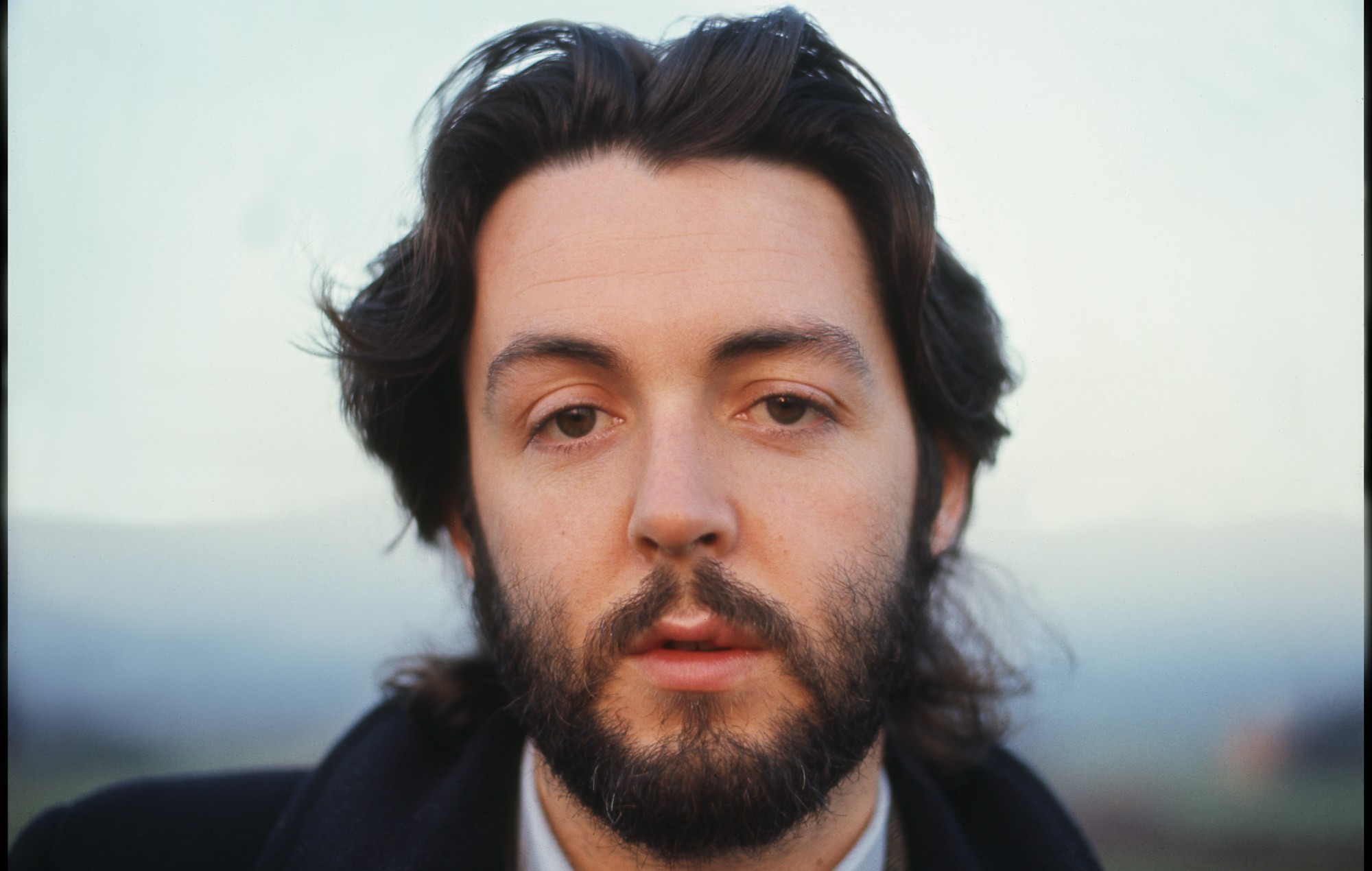 Close up portrait shot of a young white man with floppy brown hair and clipped beard, looking straight to camera