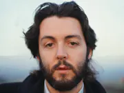 Close up portrait shot of a young white man with floppy brown hair and clipped beard, looking straight to camera
