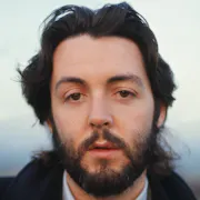Close up portrait shot of a young white man with floppy brown hair and clipped beard, looking straight to camera