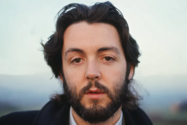 Close up portrait shot of a young white man with floppy brown hair and clipped beard, looking straight to camera