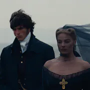 A young white man and woman in black 18th century clothing, her black veil whipping in the wind as they stand on the Yorkshire moor looking somber