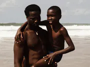 A Black man holding a young Black boy in his arm as they stand on a beach