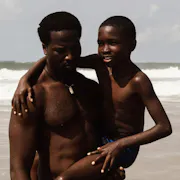 A Black man holding a young Black boy in his arm as they stand on a beach