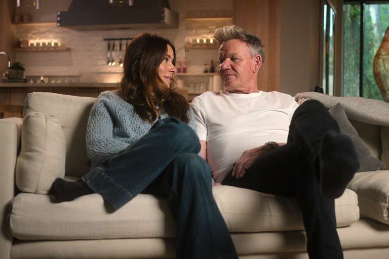A white woman and man sitting cosily on a sofa as they look at each other
