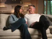 A white woman and man sitting cosily on a sofa as they look at each other