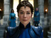 White woman, wearing a blue royal ensemble including crown, looks intensely through the screen.