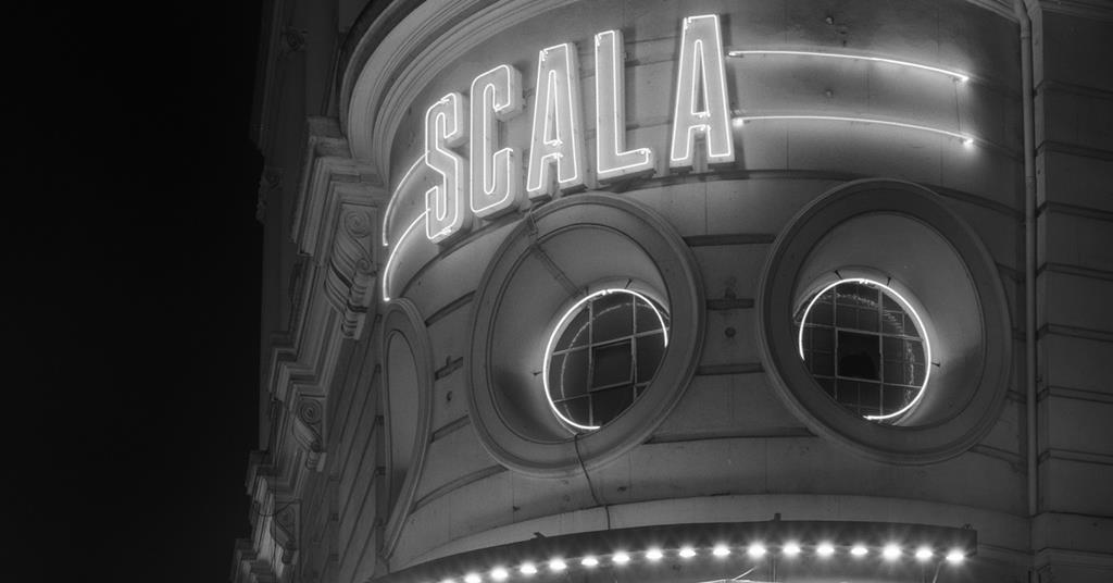 A black and white image of a building with the name "SCALA" in neon lights on the building.