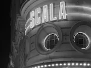 A black and white image of a building with the name "SCALA" in neon lights on the building.