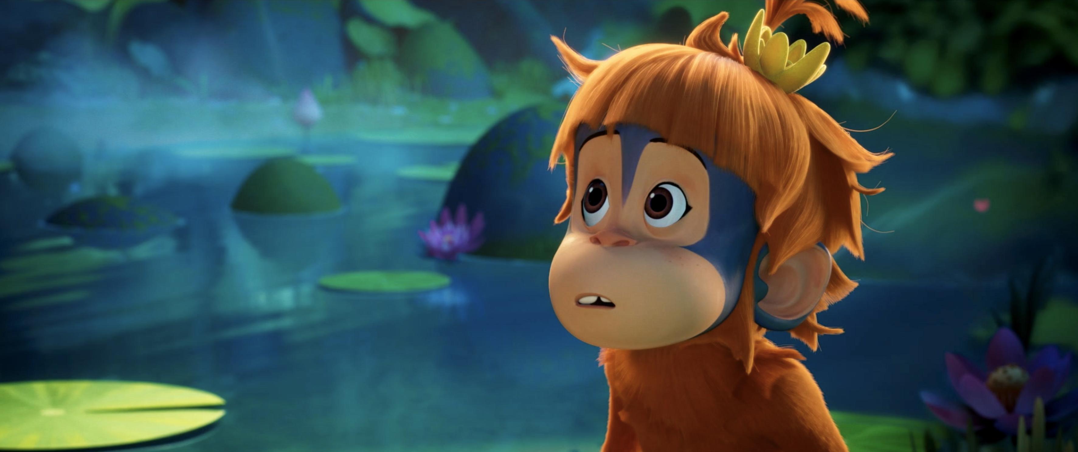 An animated, young monkey stands in front of a body of water with a look of awe.