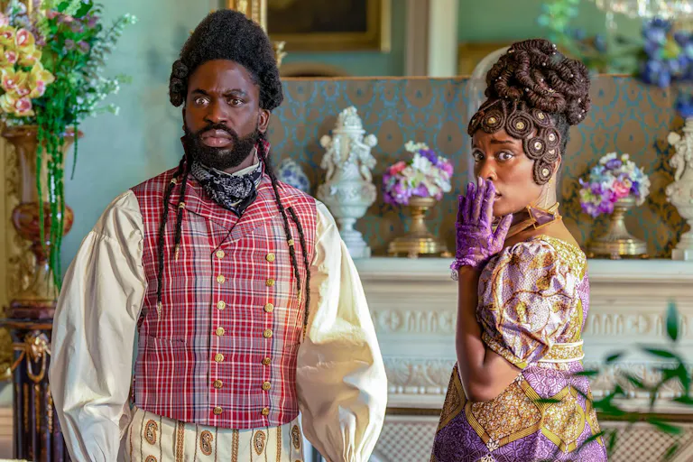 A black man and woman stand in brightly colored, regency era clothing. The woman has her hand covering her mouth.