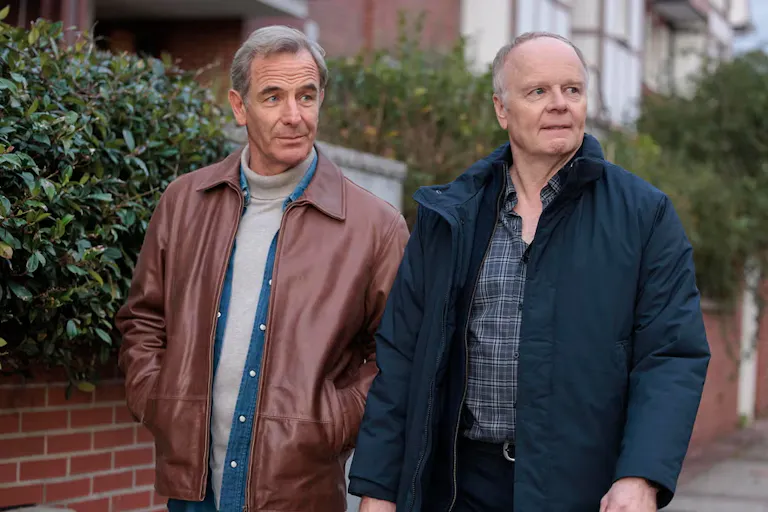 Two white man stand next to each other while walking on the pavement.
