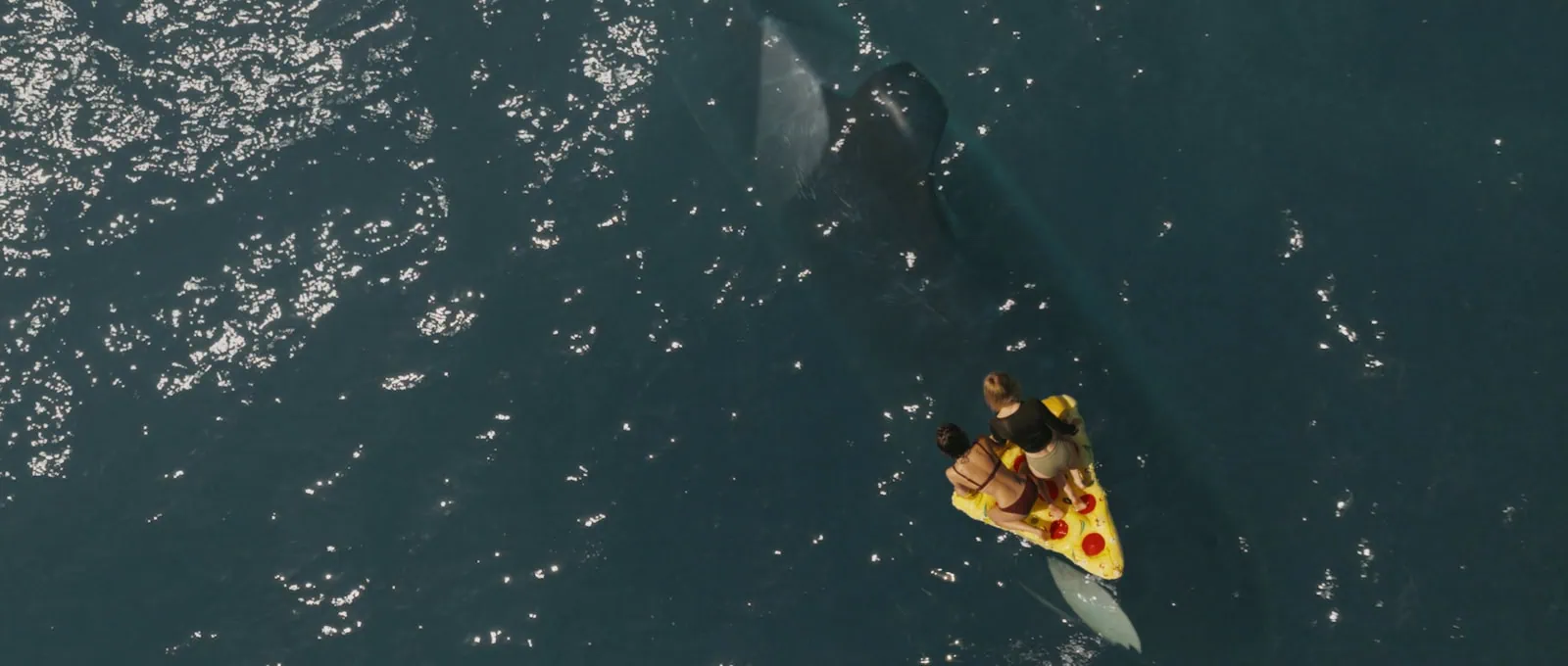A trio of people float in the ocean on a pizza shaped floating device.