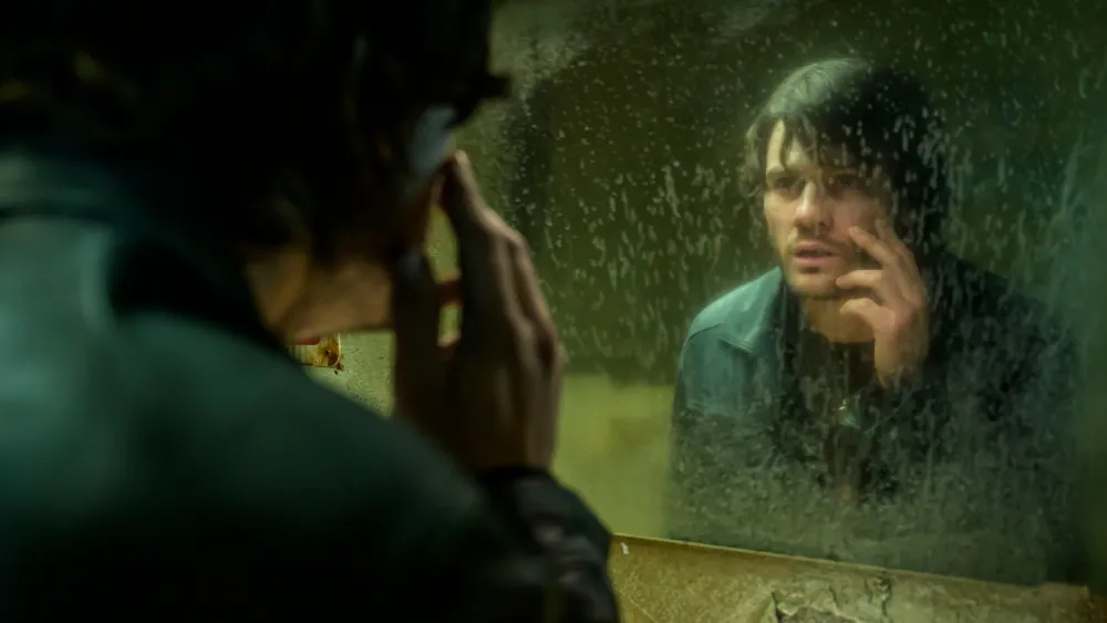 A white man looks at his reflection in the mirror while stroking his face.