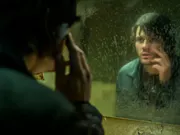 A white man looks at his reflection in the mirror while stroking his face.
