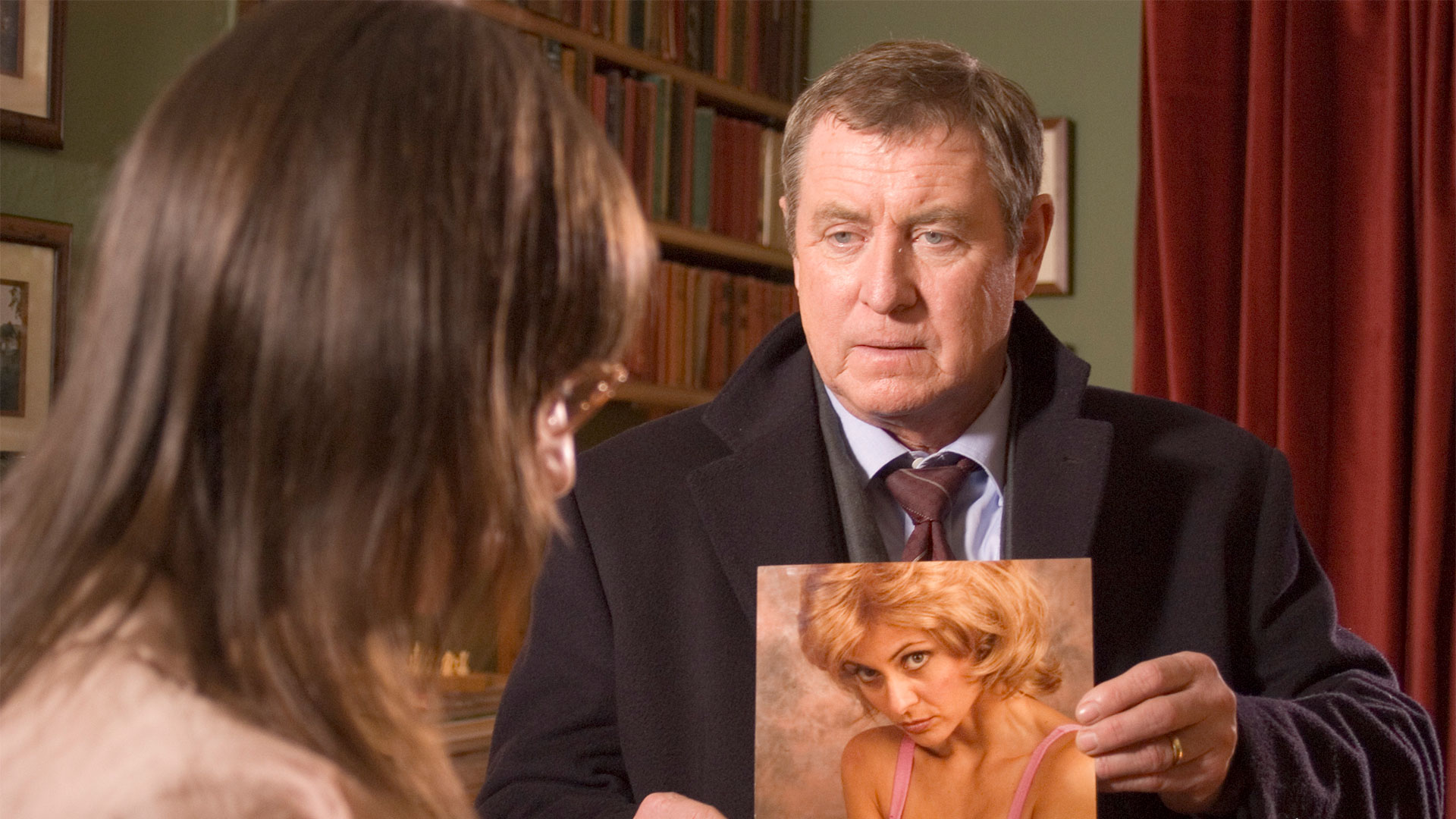 A white man holds a picture of a white, blonde woman up to another woman.