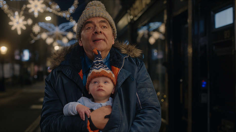 A white man stands in a beanie and puffer coat with a baby strapped to his chest, baby is also wearing a beanie.