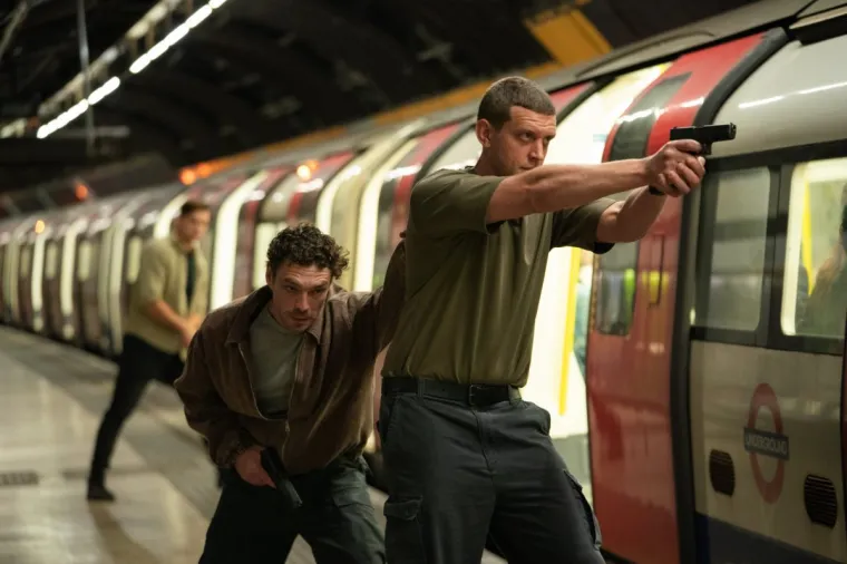 Two men stand next to the tube with guns out