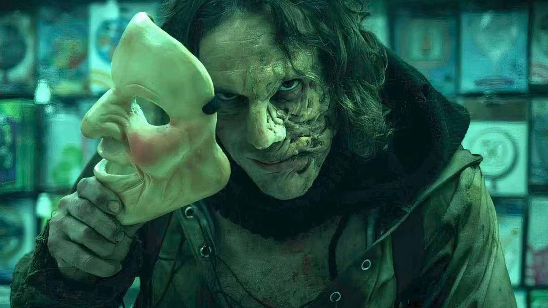 A man removes his mask revealing a slightly deformed face underneath.