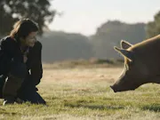 A woman kneels on the ground next to a pig in the grass.