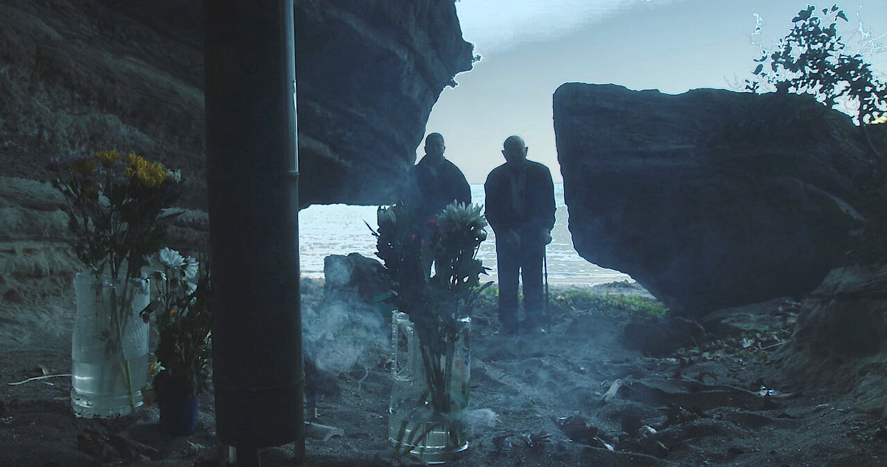 Two men stand over dirt ominously.