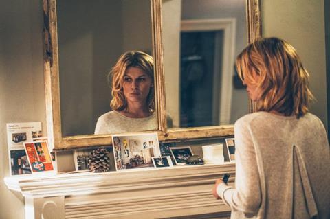 A white woman looks at herself in the mirror, hauntingly.