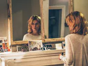 A white woman looks at herself in the mirror, hauntingly.