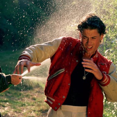 A woman gleefully sprays champagne on a shocked man wearing a sporting letterman jacket