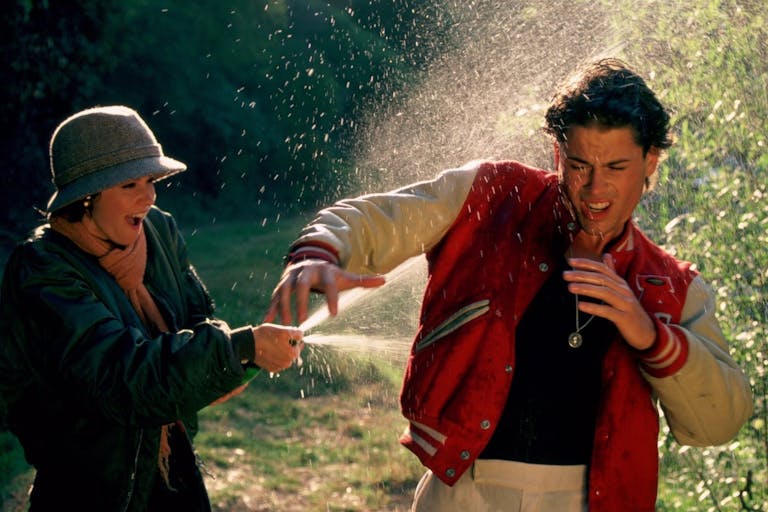 A woman gleefully sprays champagne on a shocked man wearing a sporting letterman jacket